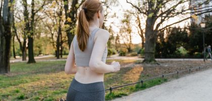 A woman jogs in a park during sunset, enjoying an outdoor fitness routine.
